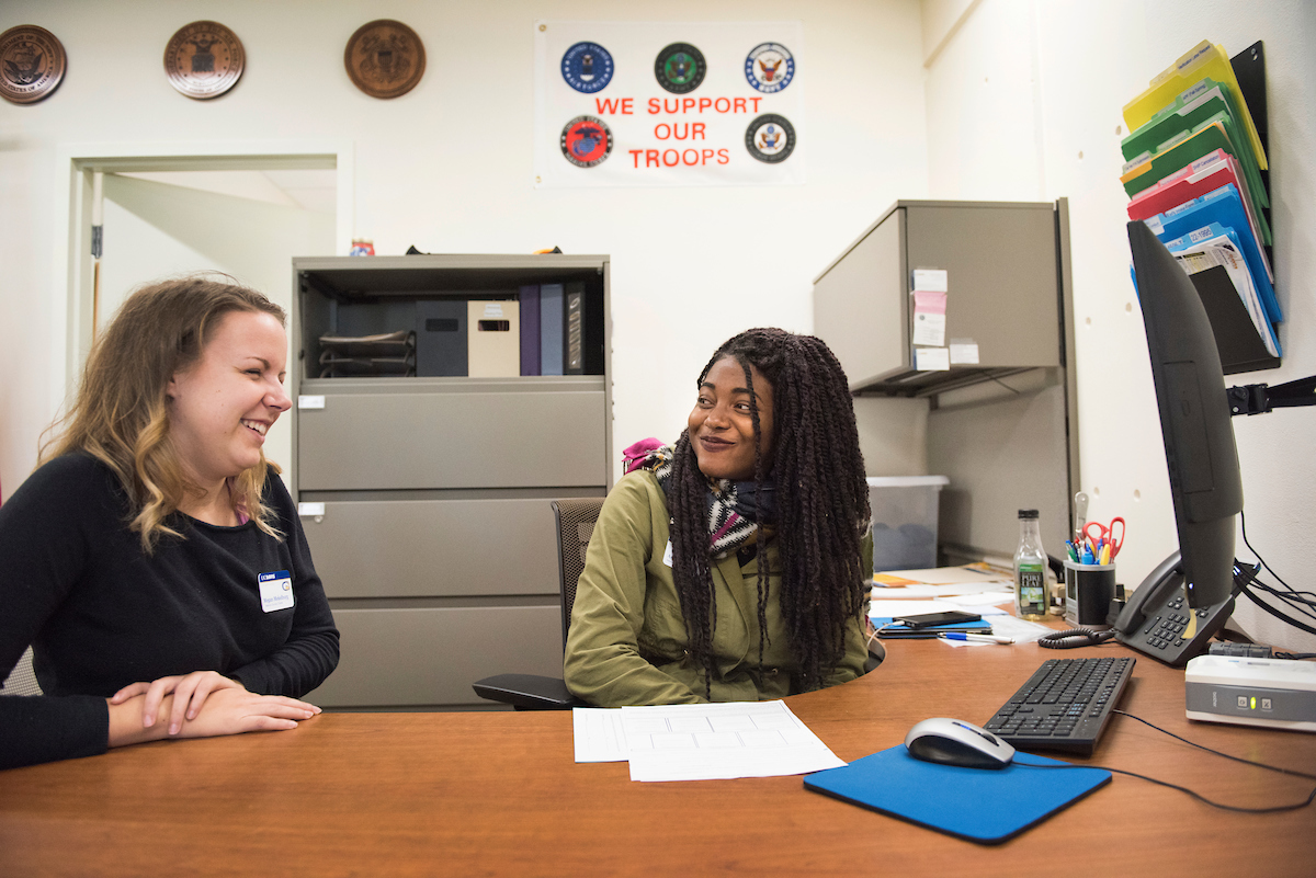 Two women talk in front of a computer. 