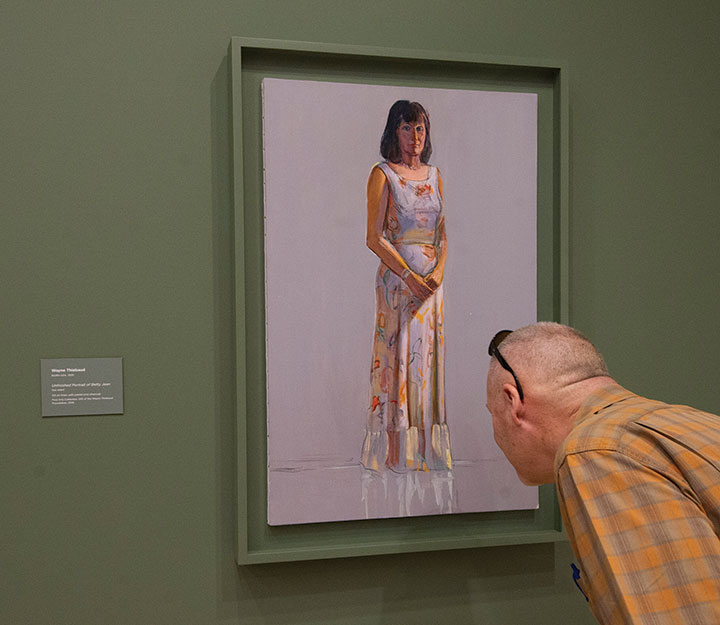 A museum guest inspects a Wayne Thiebaud painting in an exhibit