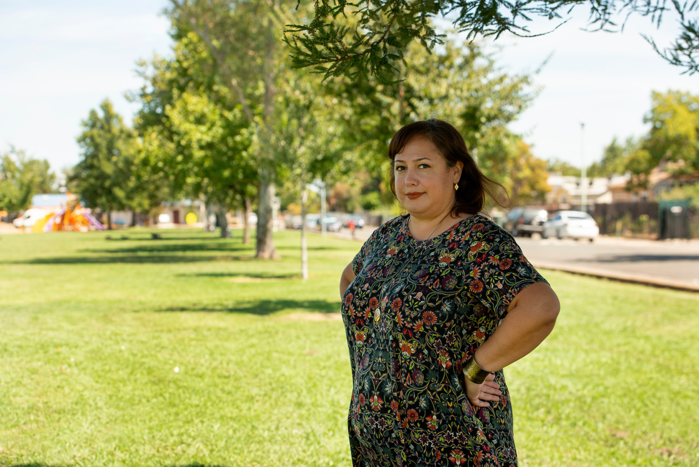 A woman stands in a green park with trees in the background