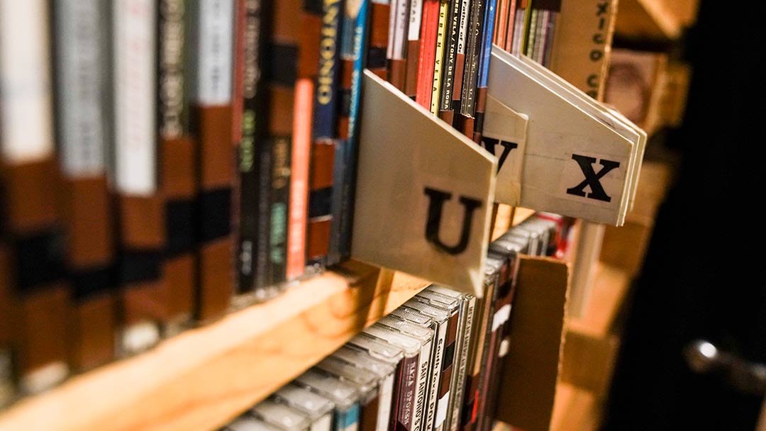 Closeup photo of a shelf with CD cases. Small tabs poke out between a few cases with the letters U and X on them, noting new sections of the collection.