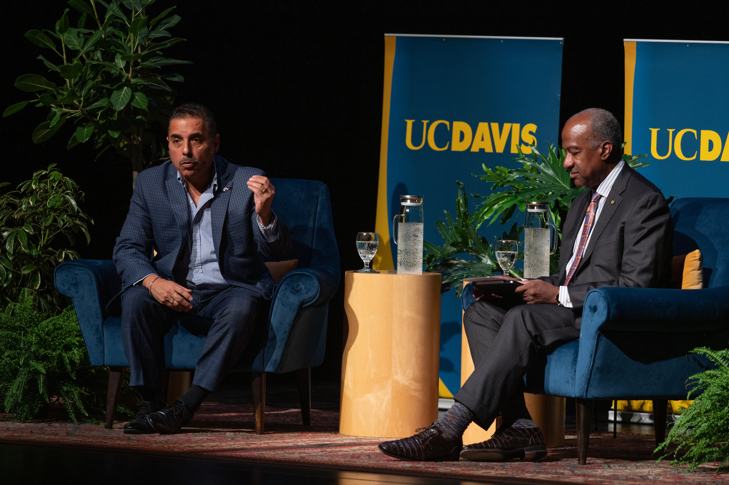 Two men in conversation on the stage of a theater in a formal, question-and-answer setting