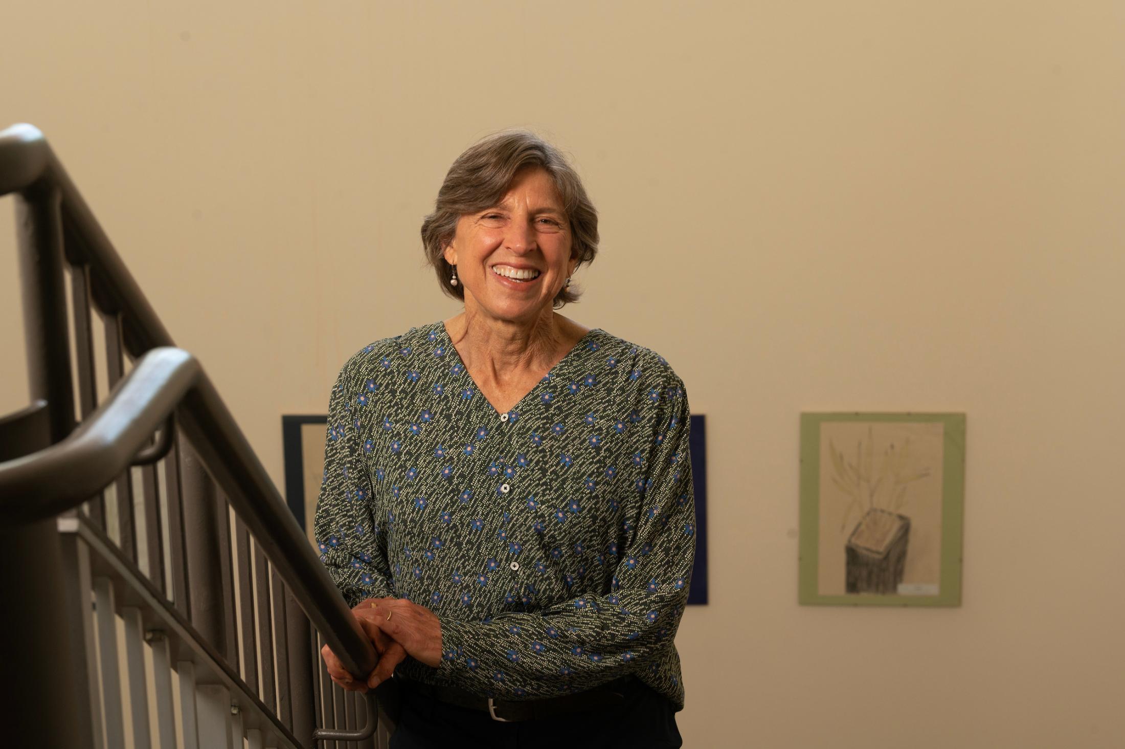 Smiling older woman leaning on stair railing against beige wall with small framed art