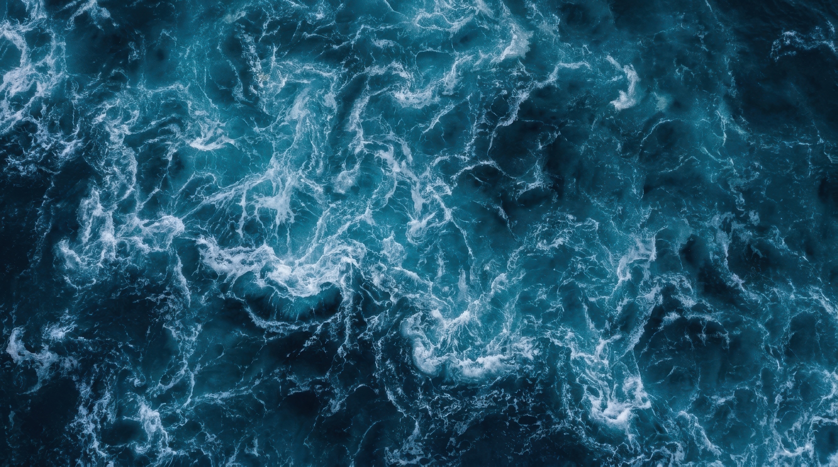Aerial view of dark teal ocean with churning foam and white-capped waves.