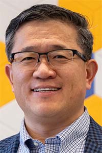 Headshot photo of smiling man wearing glasses and blue blazer
