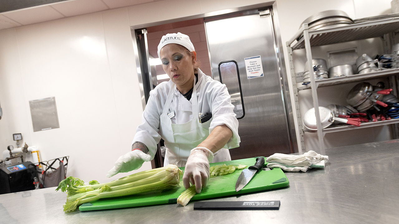 A woman in kitchen whites chops celery in Latitude's kitchen