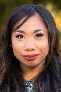 Close-up headshot of a smiling woman with long dark hair, blurred outdoor background