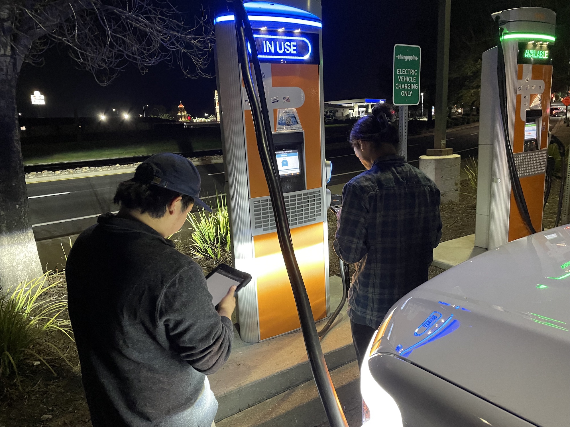 UC Davis students Joshua Bang, left, and Brian Olszewski, right, stand in front of a Charge Point electric vehicle charging station at night while charging a Ford F-150 Lightning. They are helping researchers test the reliability of thousands of electric vehicle charging stations across California. (Amy Quinton / UC Davis)