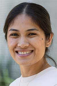 Smiling woman with dark hair pulled back, wearing white top, blurred background