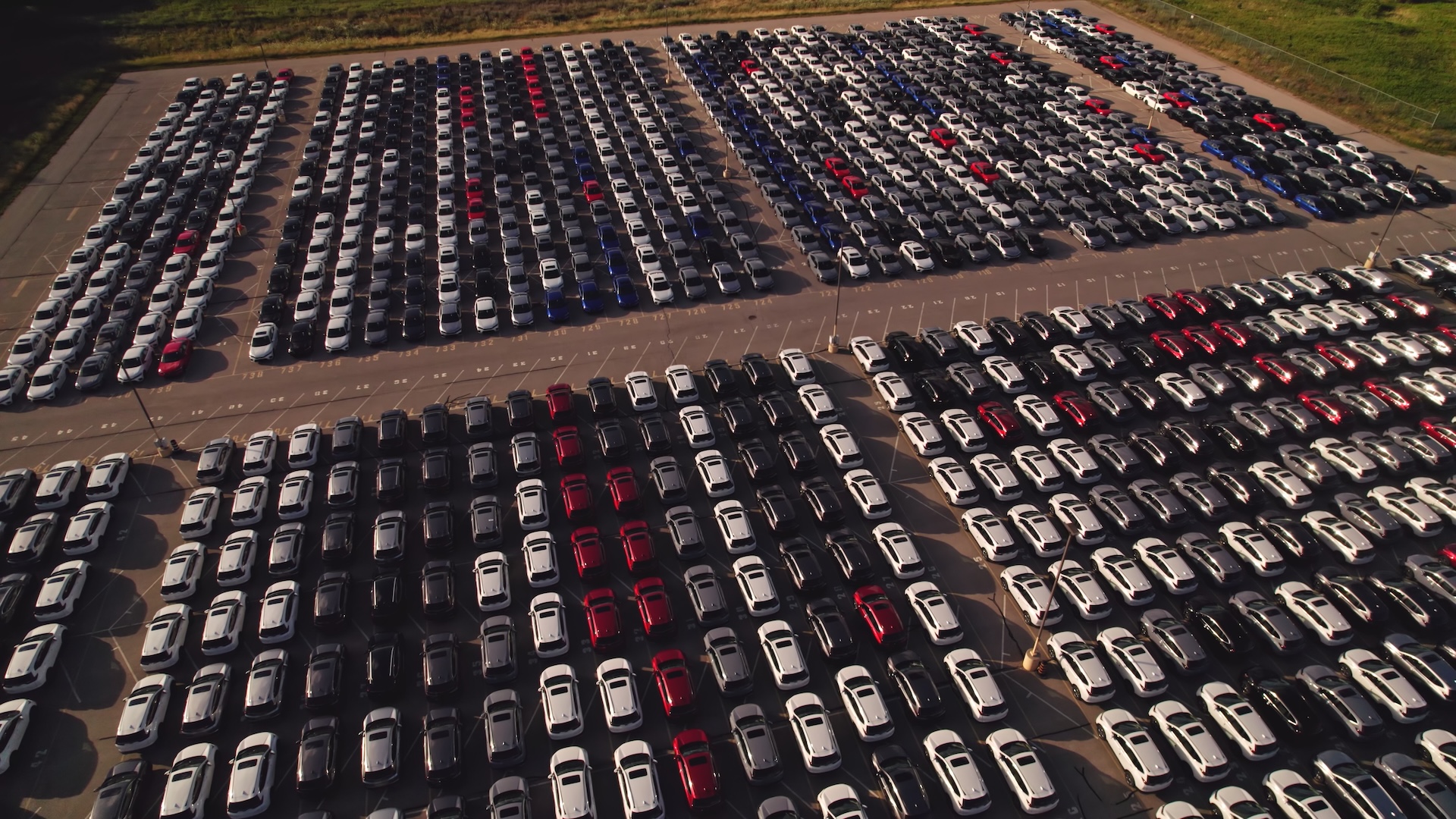 Aerial view of a large parking lot filled with rows of cars in various colors.