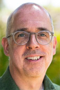 Smiling bald man wearing round glasses, portrait photo against green blurred background