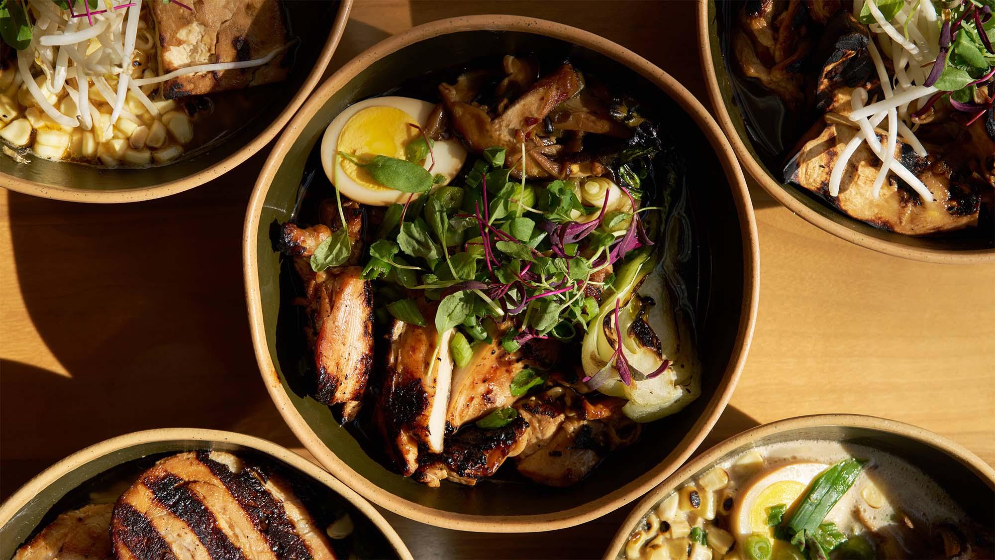 Warm-lit bowls on wooden table, central bowl of grilled shrimp, herbs and lemon.