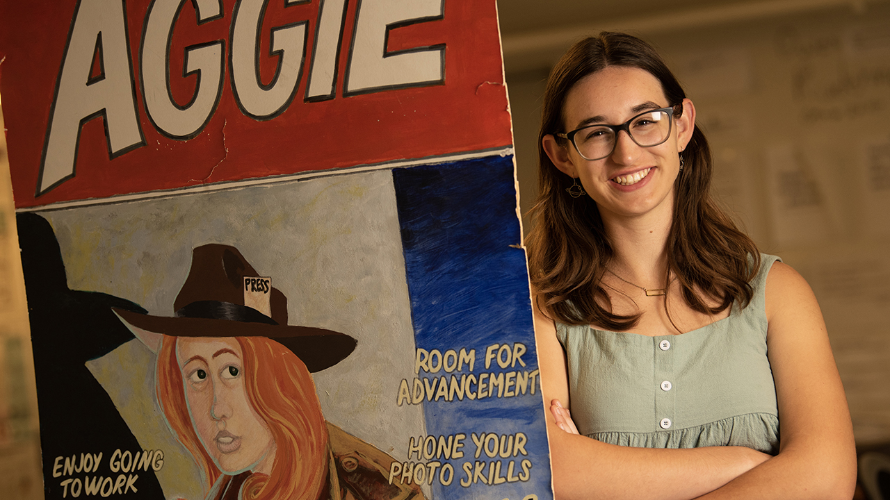 Sonora Slater stands beside a large recruitment poster for The California Aggie.