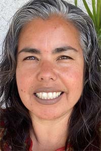 Close-up photo of smiling woman with salt-and-pepper hair and green plant behind