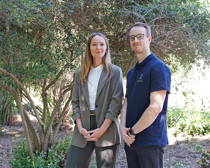 Young woman in gray blazer and man in navy polo standing in a shaded garden, photo