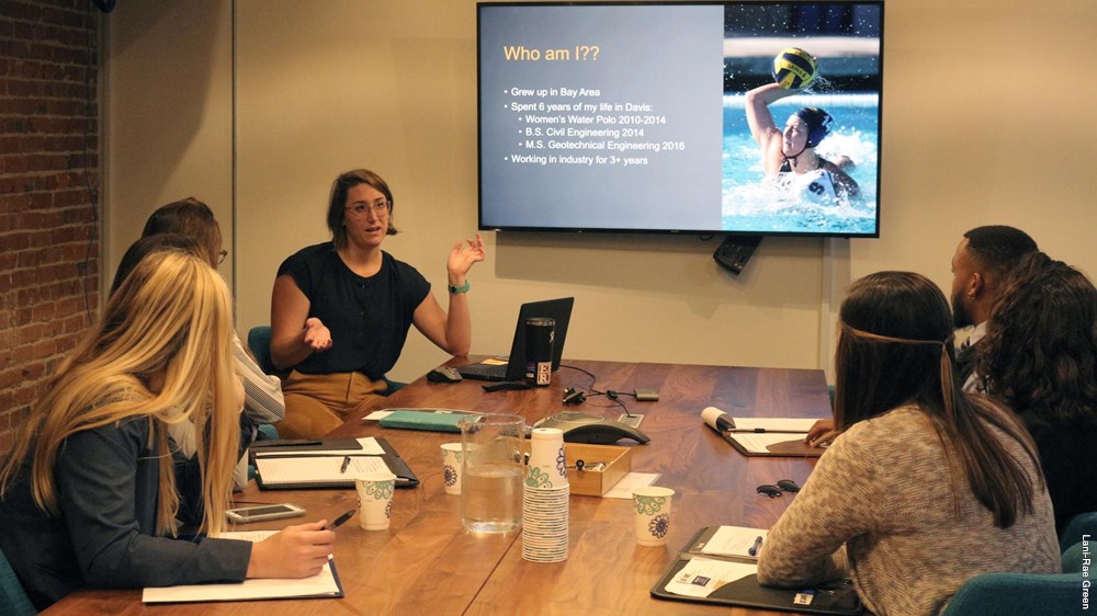 Woman speaks to students around conference table.