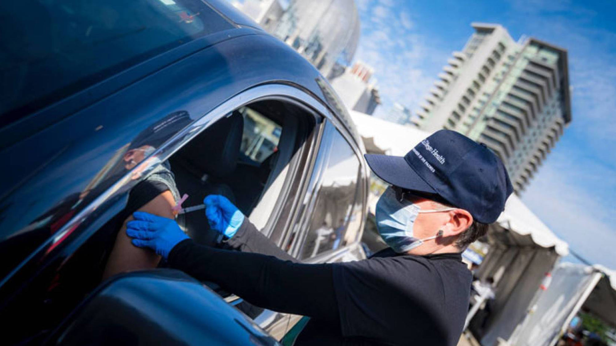 Woman in face mask gives vaccination to person in a car