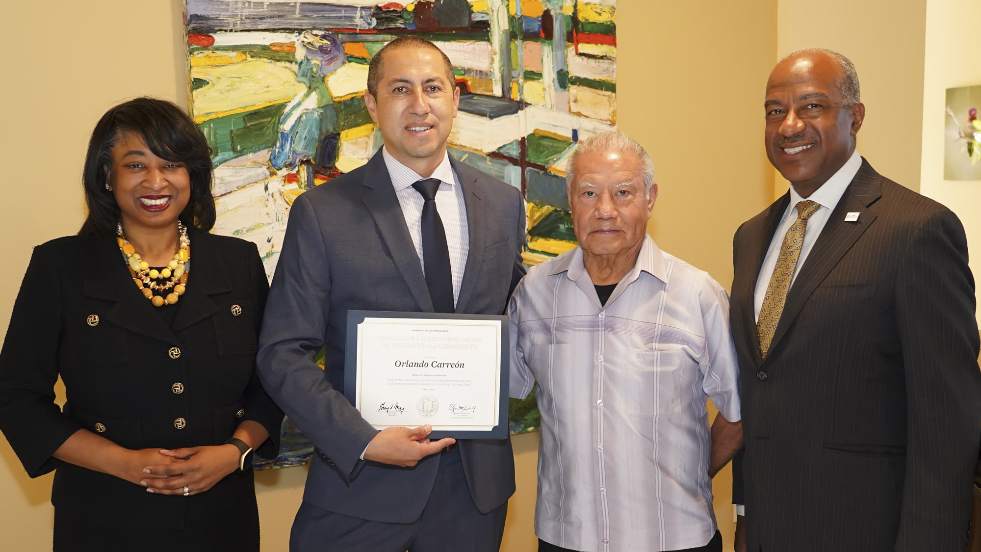 Four people in a line, posed, one holding certificate