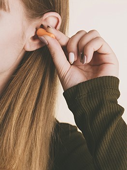 A person inserts an earplug into their ear.