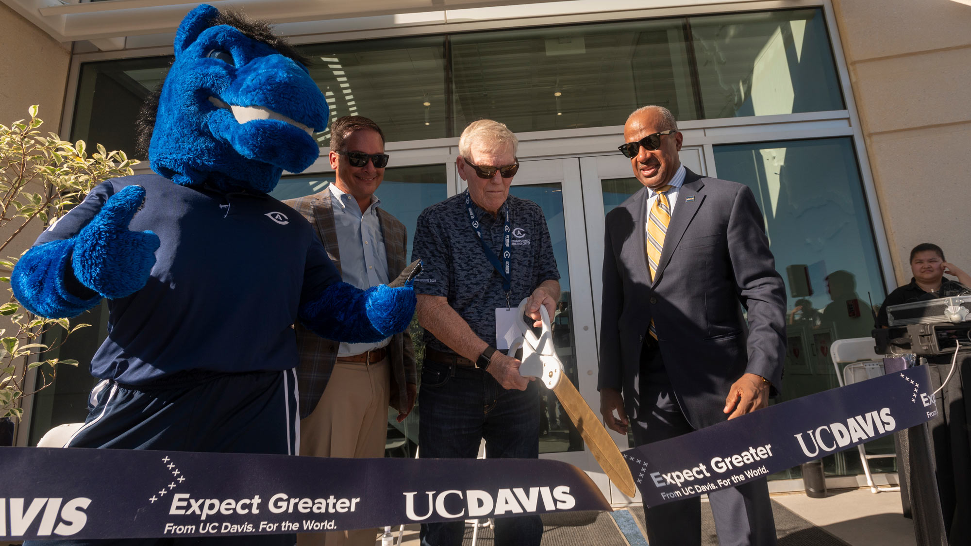 Three men cut ribbon with giant scissors