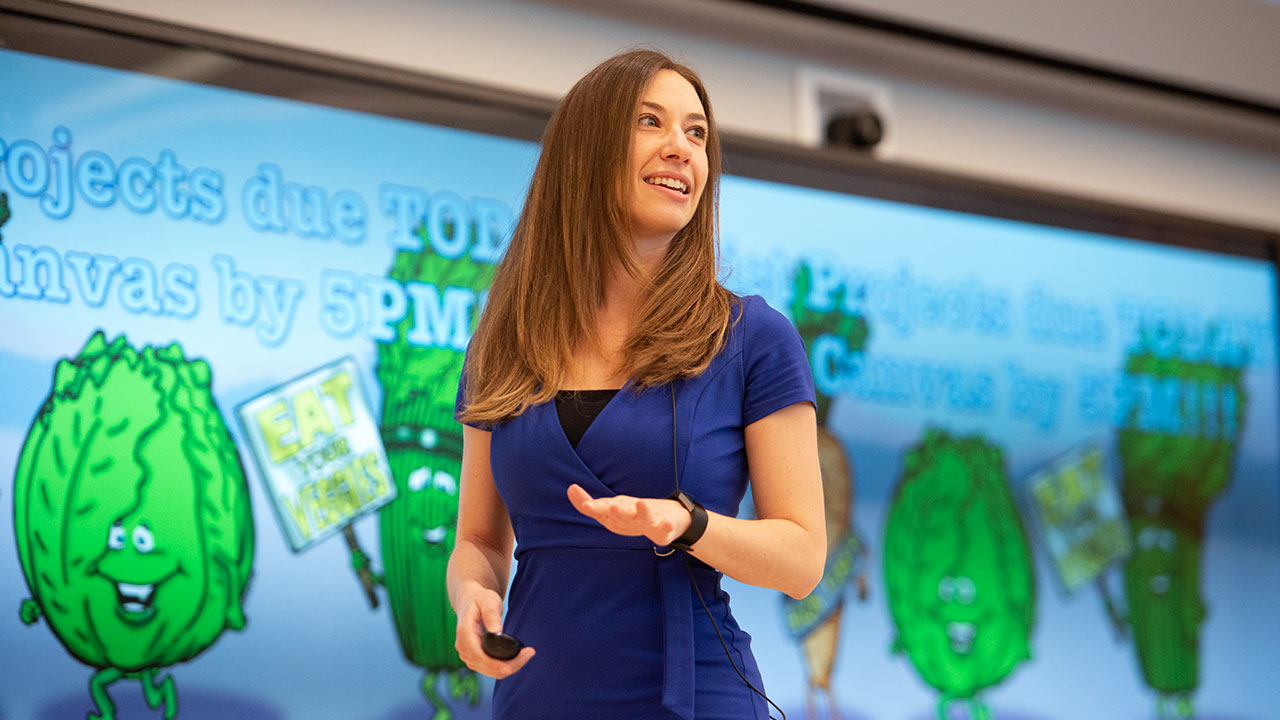 Debbie Fetter stands in front of a slide with cartoon images of green vegetables.