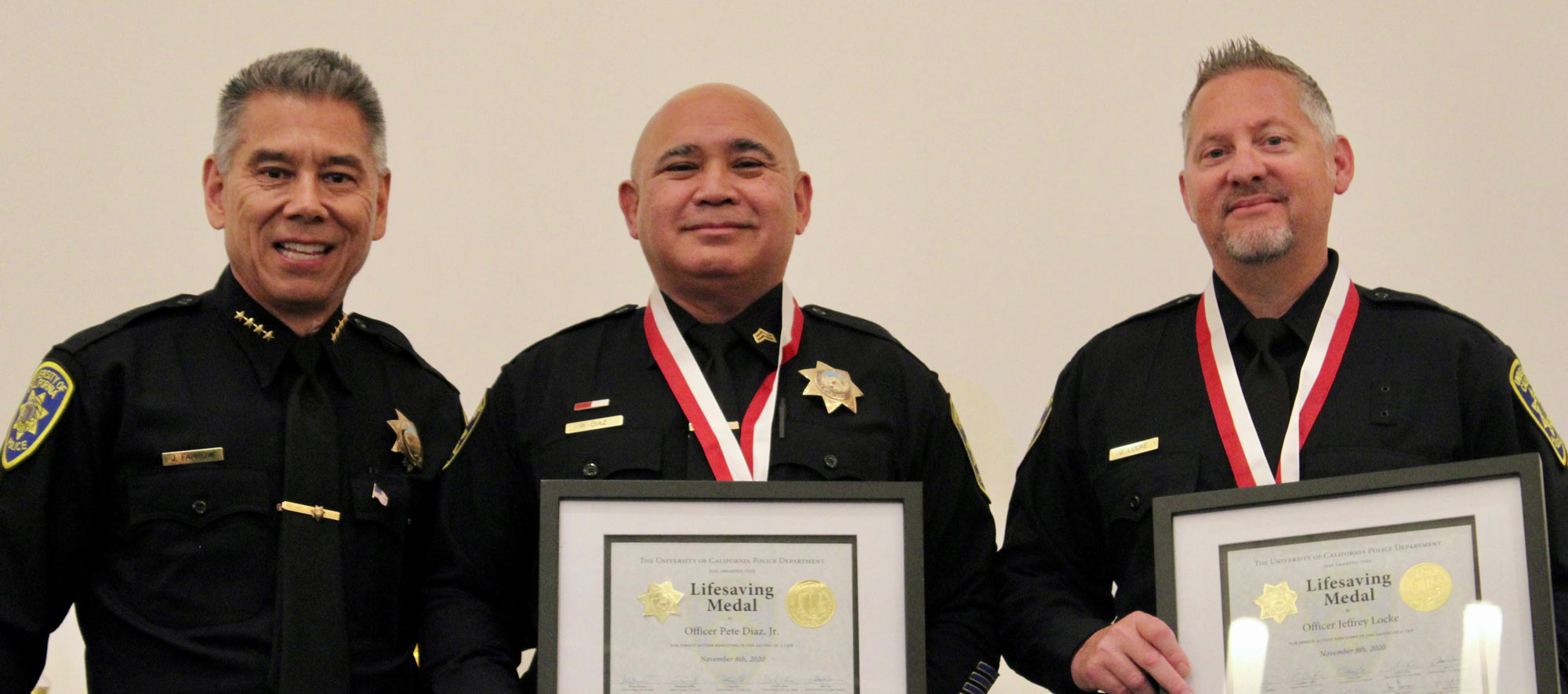 3 men in police iniforms, two holding certificates and wearing medals