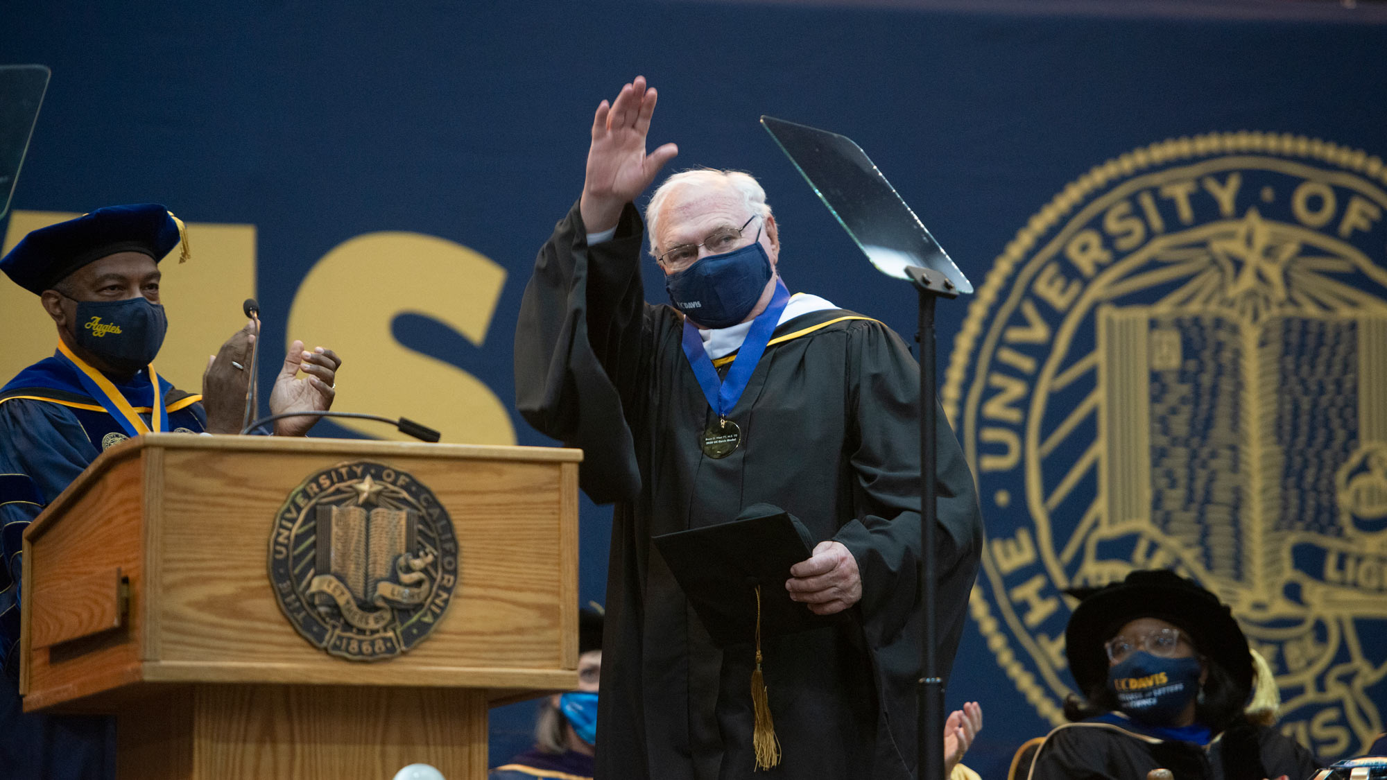 Alumnus wearing medal, acknowledges audience.