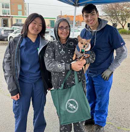 Person holds pet while posing for photo with two clinic volunteers