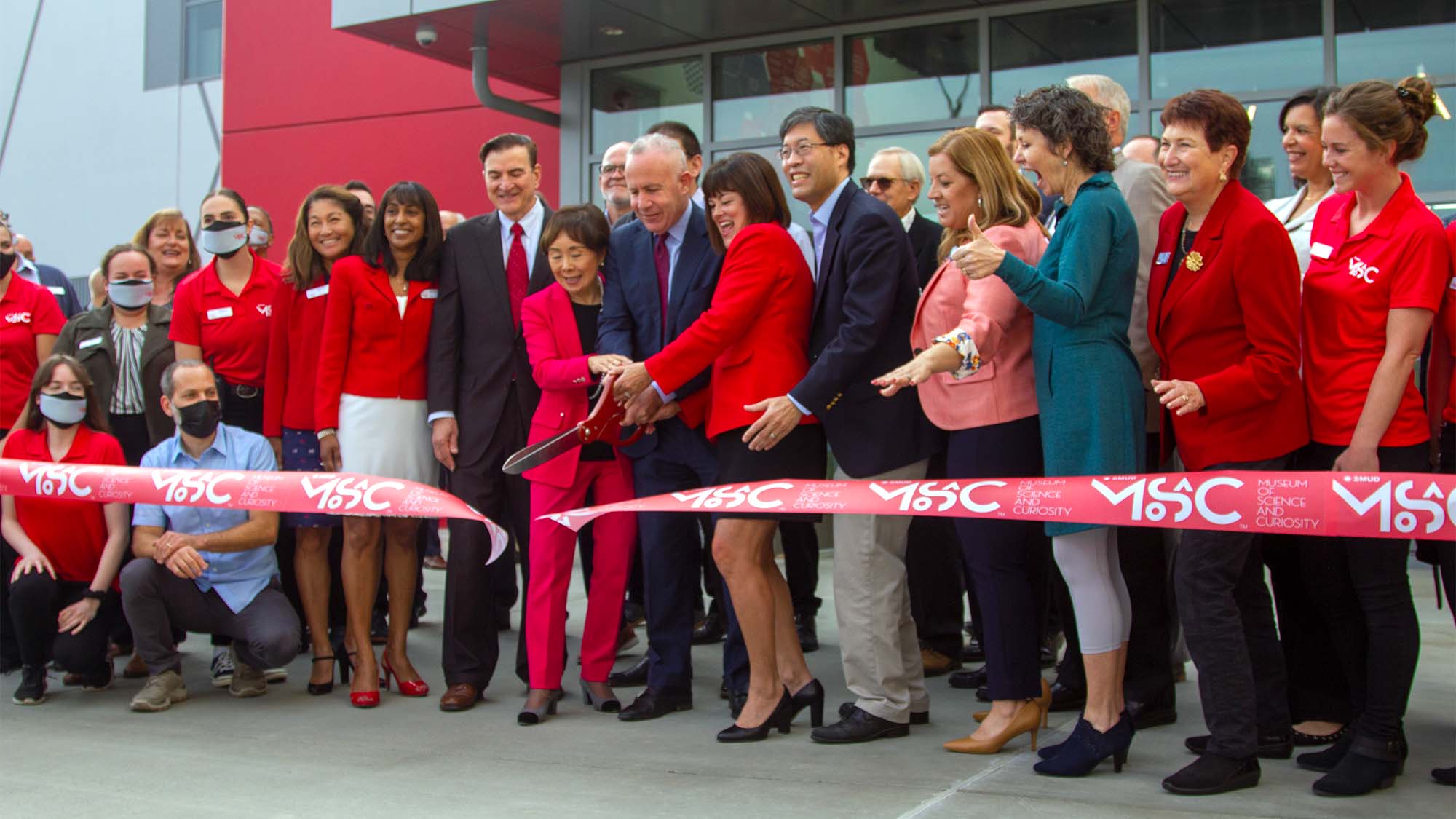 Large group of people cut a ribbon at the MOSAC.