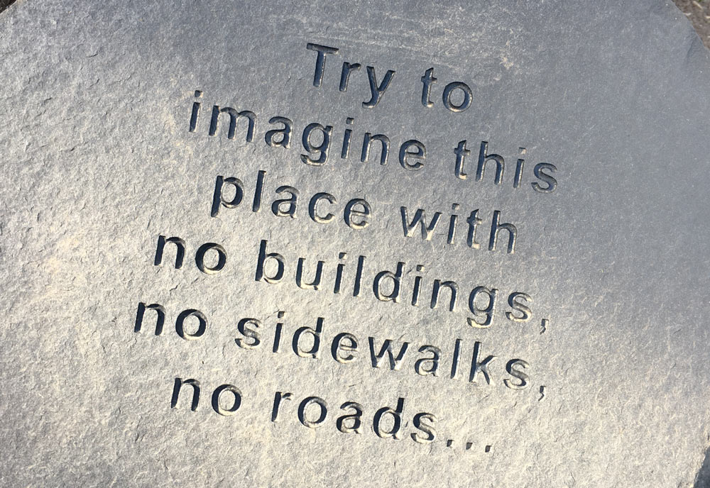 Top of basalt column with inscription, "Try to imagine this place with no buildings, no sidewalks, no roads ..."