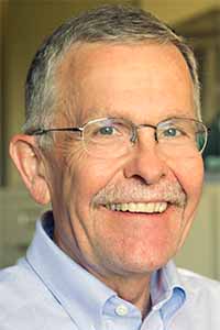Smiling man with gray hair, mustache and glasses wearing a light blue shirt