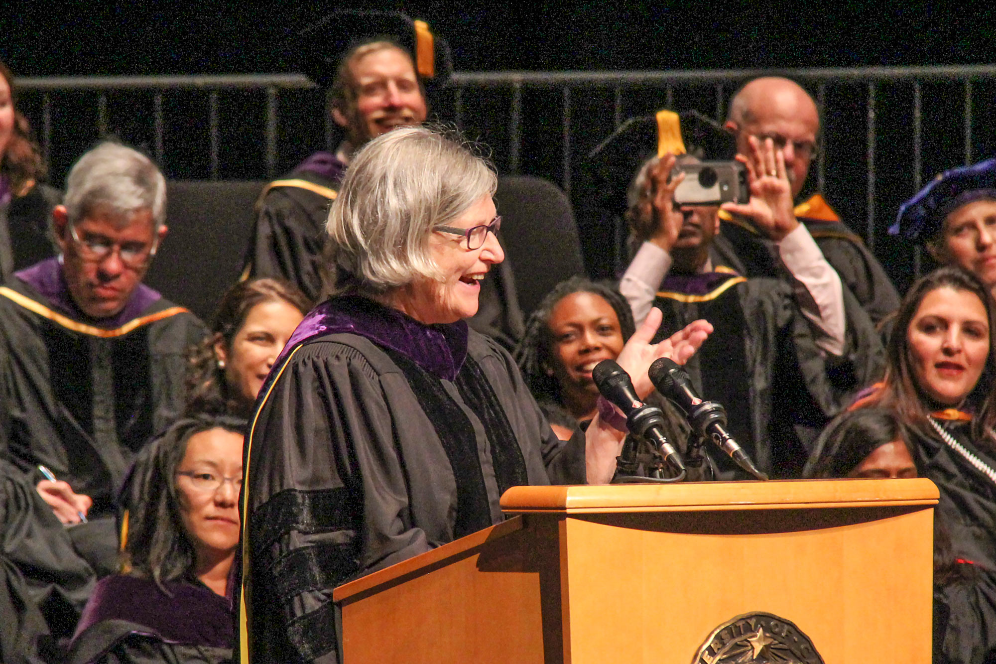 Woman in commencement regalia, speaking at podium