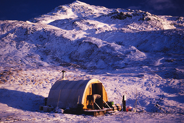 Snow-covered landscape with a small tent and rugged mountains in the background.