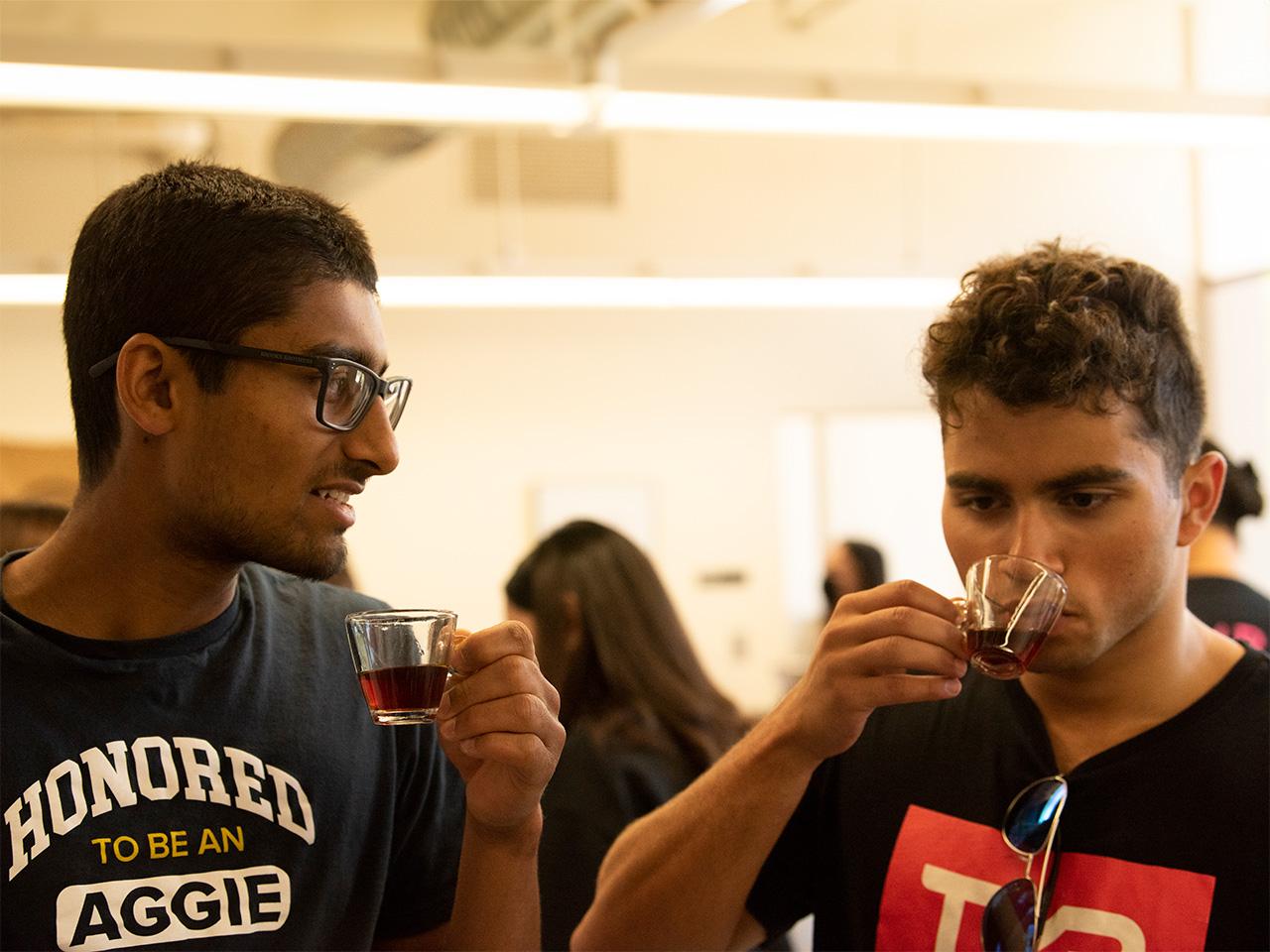 Two students concentrate as they taste coffee in small glasses.