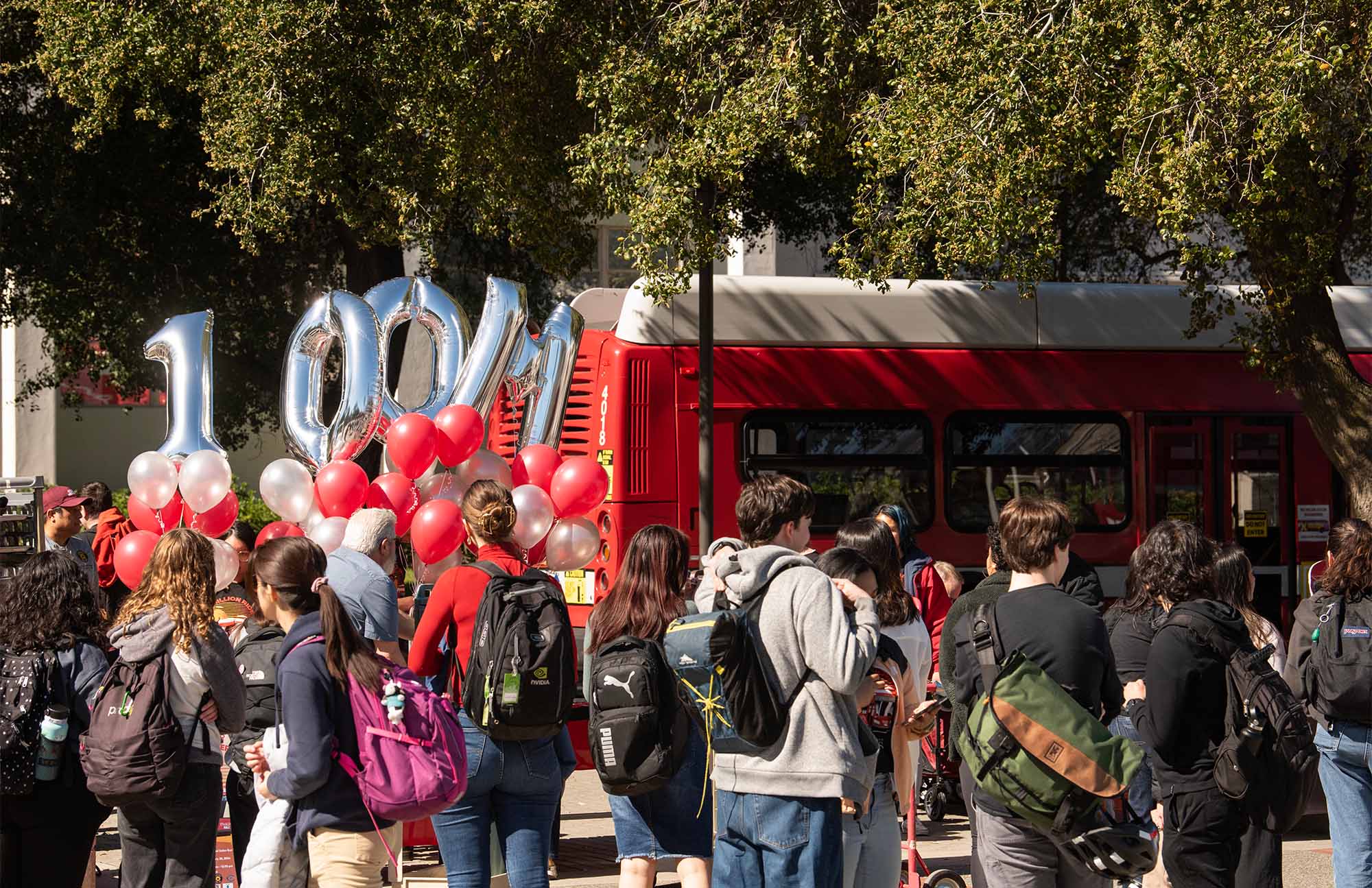 Silver balloons spell "100M" near red Unitrans bus.