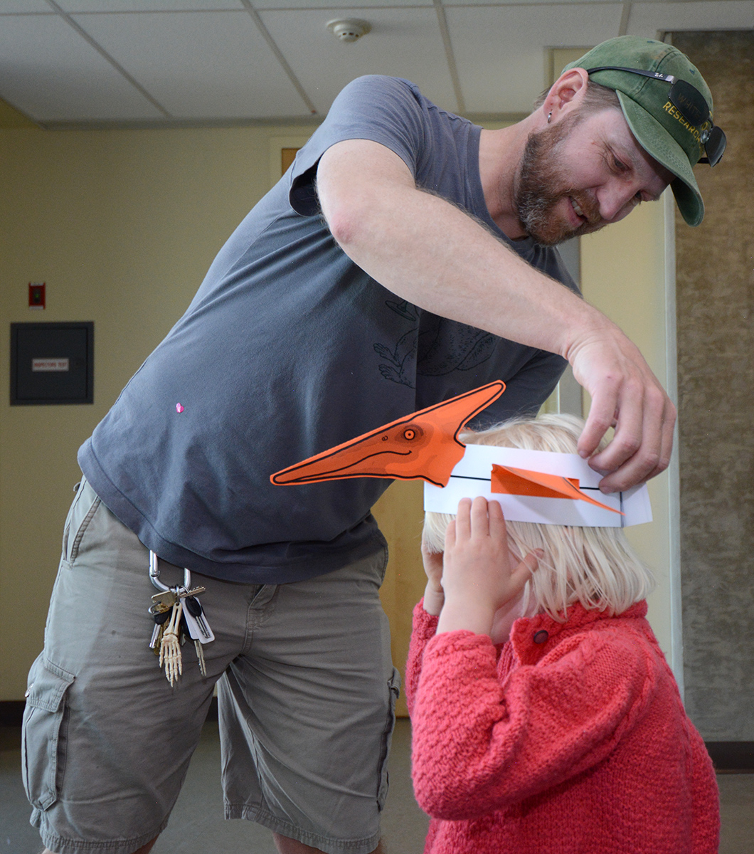 Earth and Planetary Sciences professor Eric Cowgill fits a dinosaur hat on his daughter, 4-year-old Simone, at Picnic Day. (Cody Kitaura/UC Davis