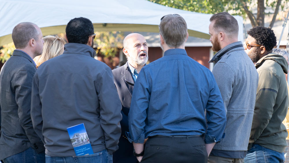 Man addresses group of men gathered in semicircle around him.