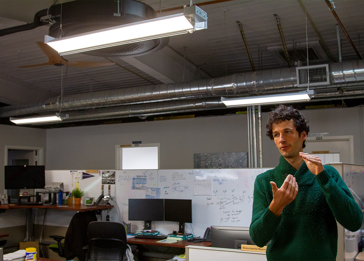 Man in green sweater stands in office.