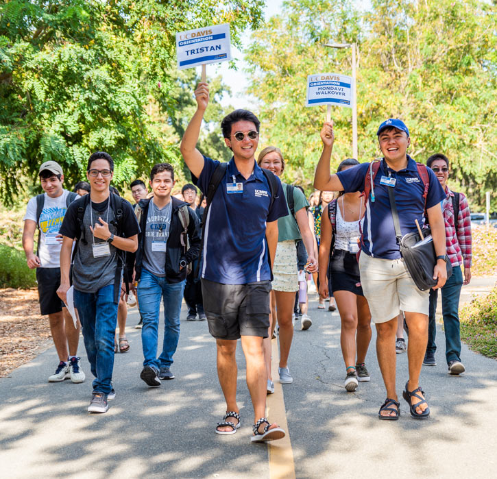 Orientation leader holds sign with his name on it, new students follow him.