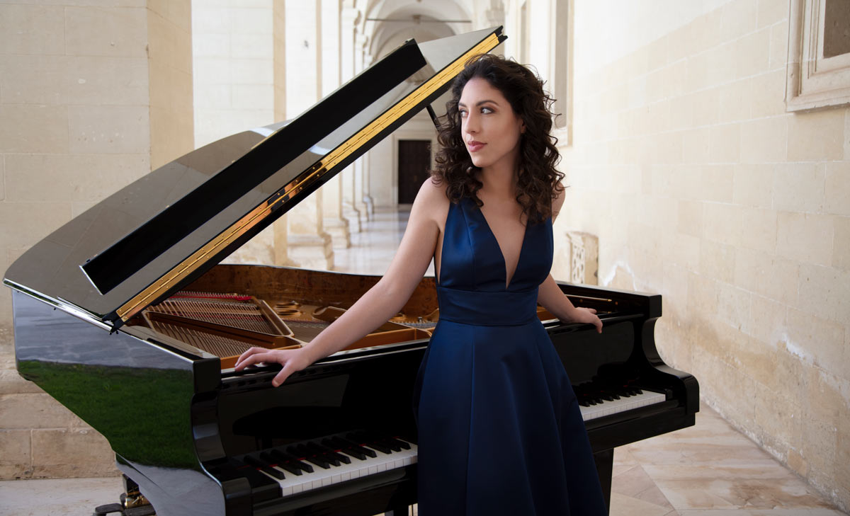 Woman stands next to piano.