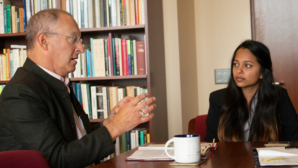 Ralph J. Hexter in conversation with a job shadow student, at table.