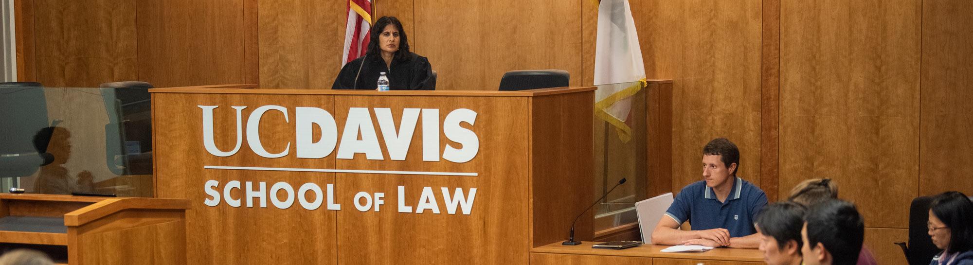 UC Davis School of Law sign on wood paneling; masked speaker at podium, seated panelists