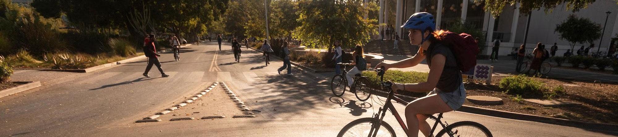 Cyclist in helmet rides across sunlit urban plaza at sunset, casting long shadows