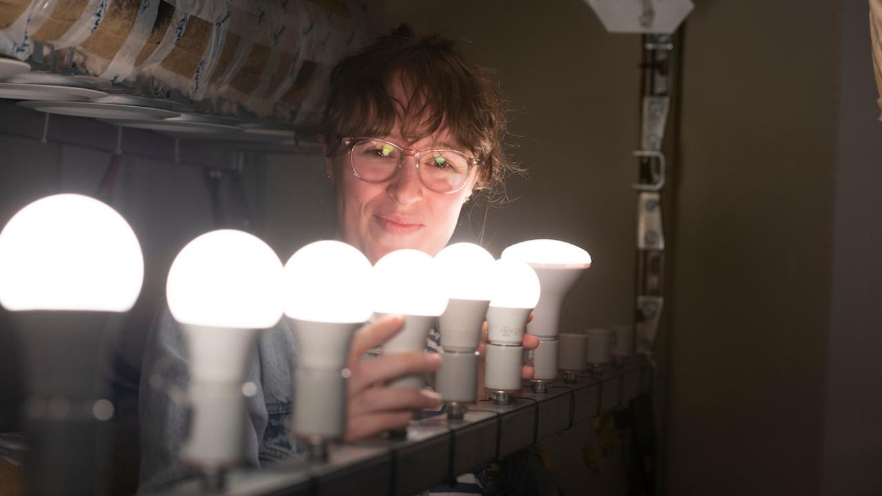 A smiling student screws on a row of bright light bulbs.