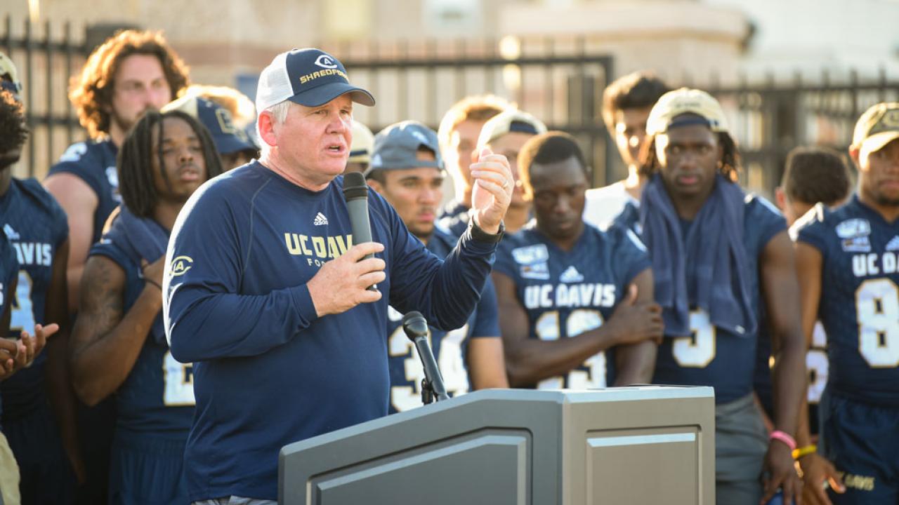 Coach Dan Hawkins at podium, team behind him, at Football Fan Fest