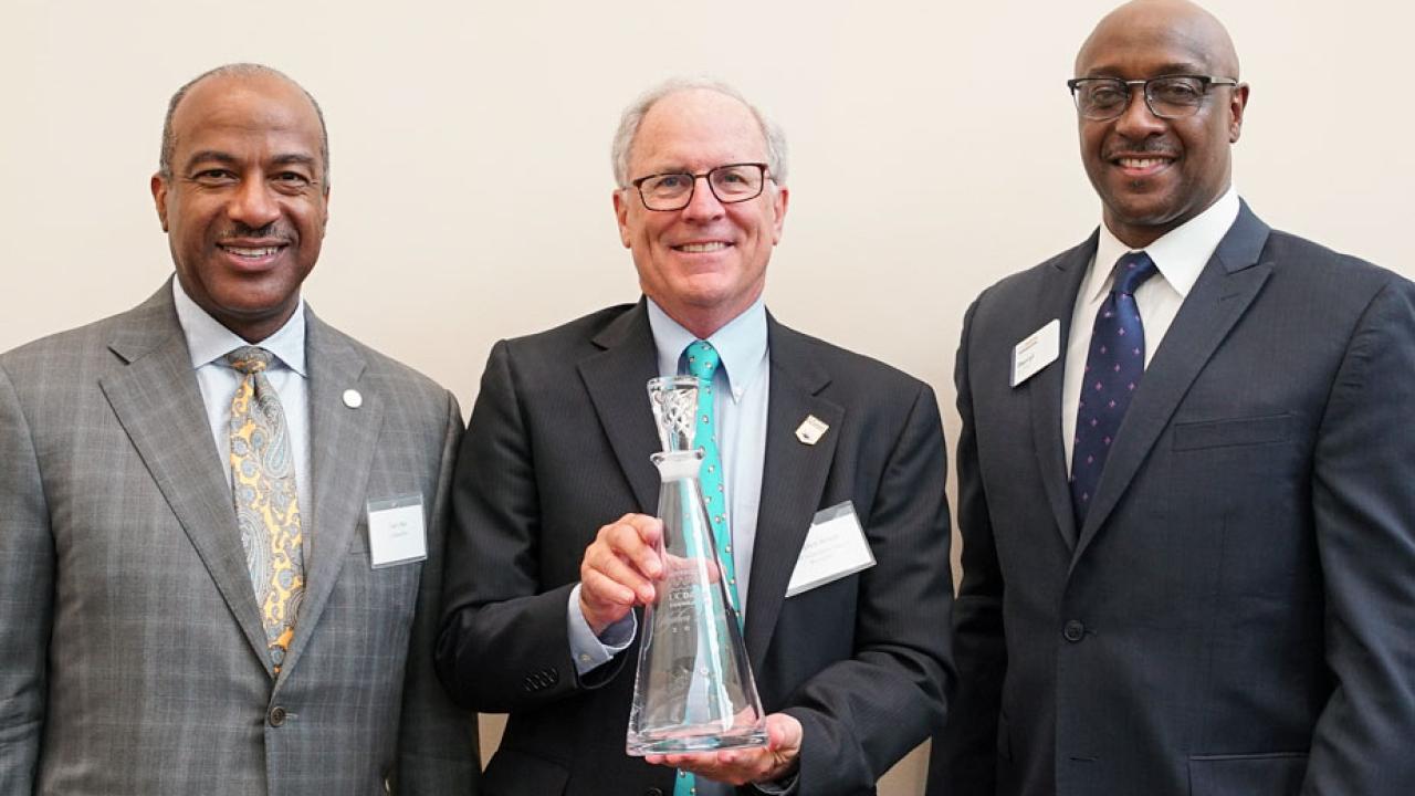 Three men pose for photo, award winner in middle holds decanter award.