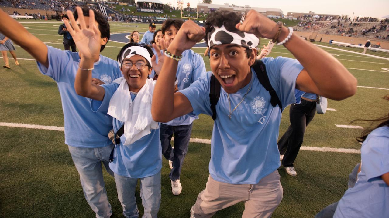 Young people in light-blue shirts cheering exuberantly on a sunny football field