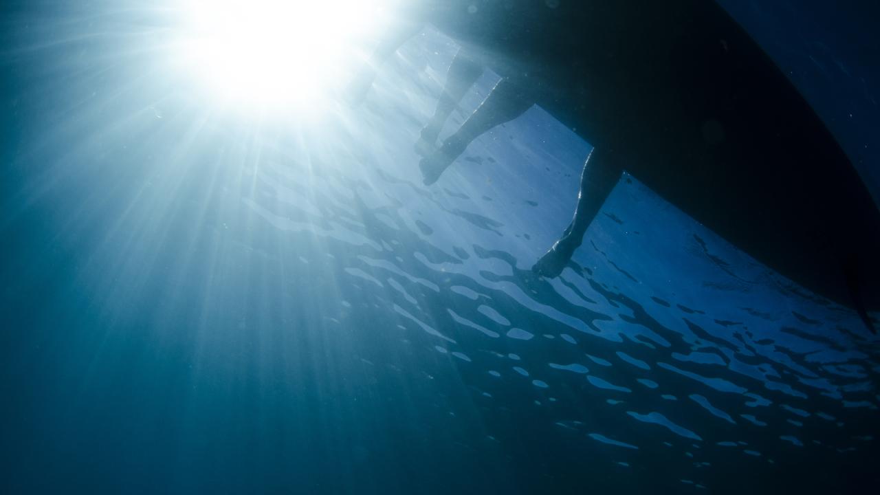 photo taken underwater shows light entering water as shadowy legs dangle from a paddleboard at Lake Tahoe