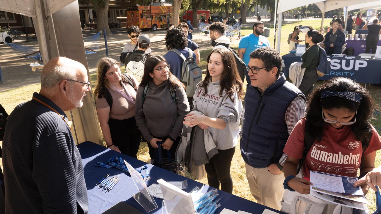 Luis Carvajal-Carmona and three students at a booth at the Graduate and Law School Fair on the Quad.