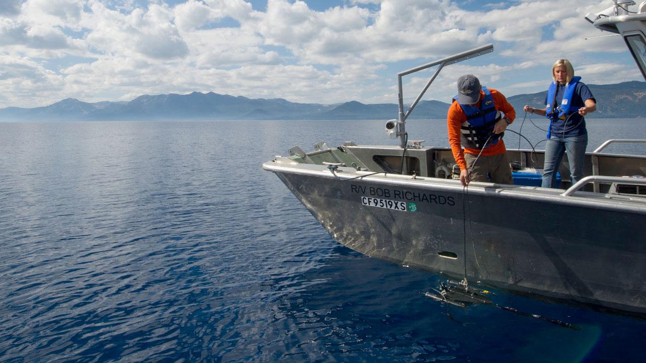 Two researchers take a water sample from their boat in the middle of Lake Tahoe.