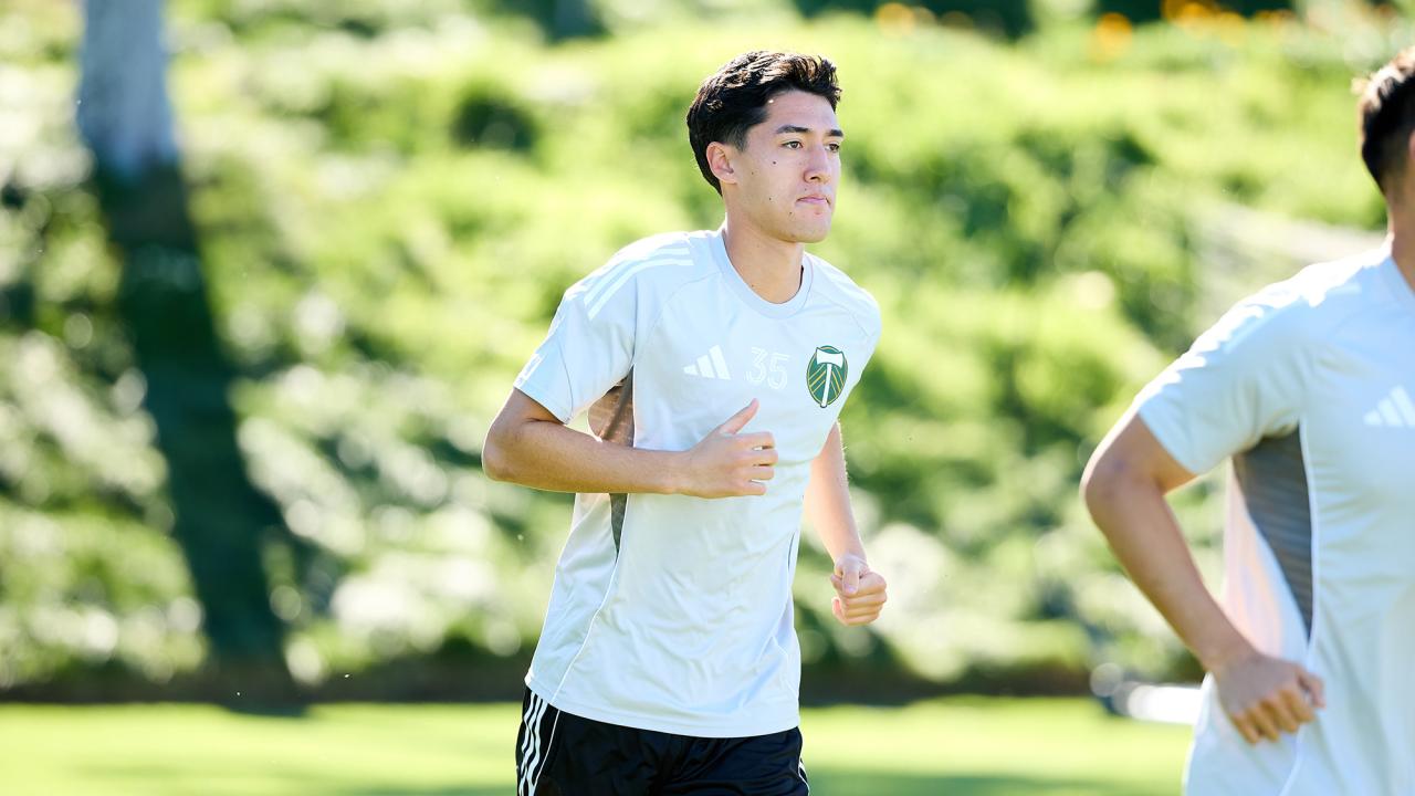A young athlete jogging on a bright green field, wearing a white jersey and black shorts.